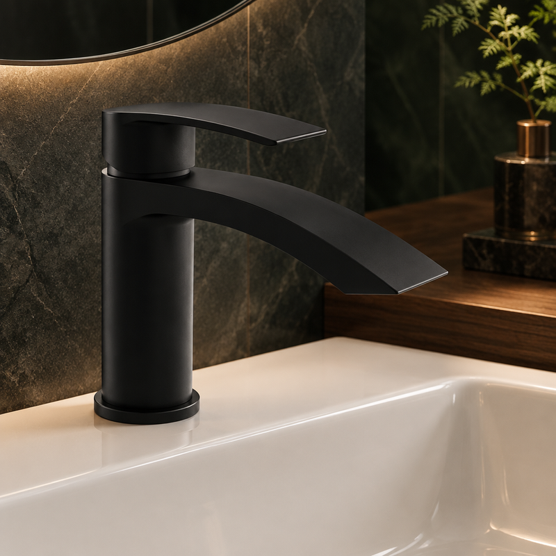 Kartell Curve Nero matt black basin mixer tap with curved spout installed on a white basin against dark bathroom tile and wood accents