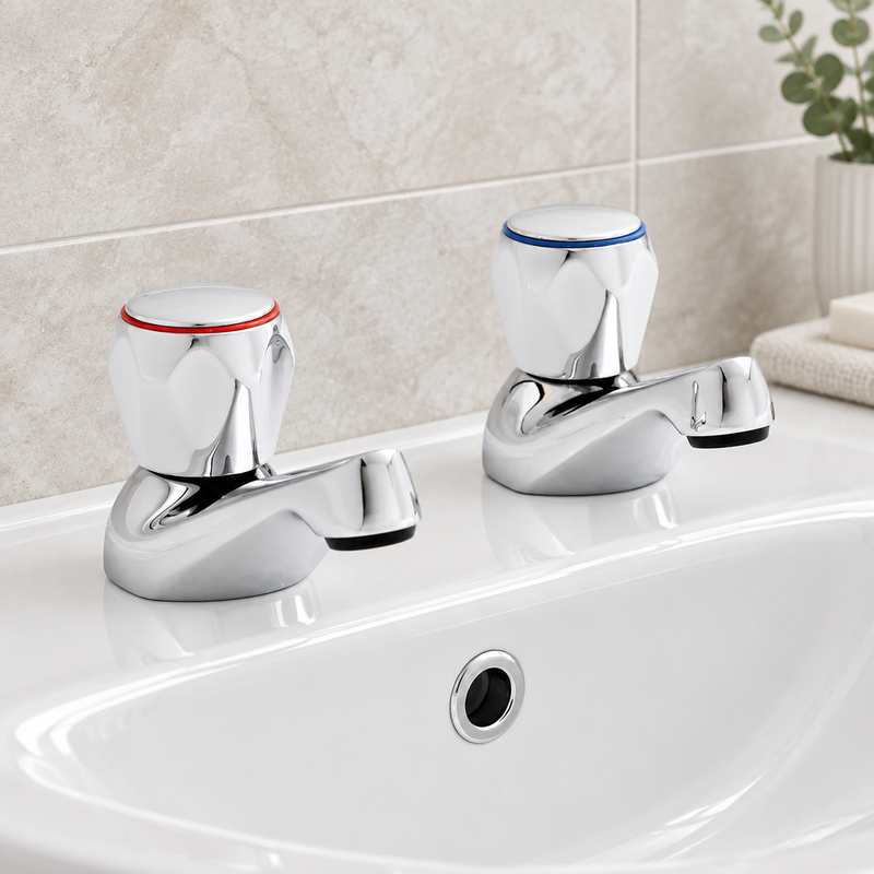 Pair of chrome basin taps with red and blue ceramic handles installed on a white bathroom basin